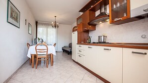A compact kitchen with wooden cabinets, a dining table with chairs, and a chandelier. - Seaside Serenity Flat With Outdoor Pool (Rosolina)
