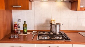 A kitchen with a stove, a pot, a bottle of olive oil, and two shot glasses on a wooden countertop. - Seaside Serenity Flat With Outdoor Pool (Rosolina)