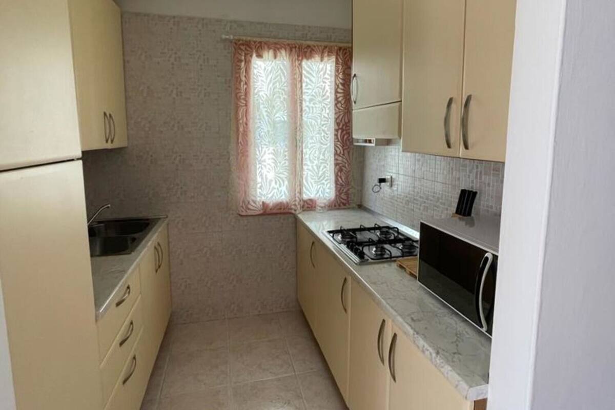 A compact kitchen with beige cabinets, a gas stove, and a window with patterned curtains.