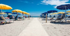A beach with rows of sun loungers under umbrellas, a wooden walkway, and the ocean in the background. - Spacious Apartment With Terrace in Rosolina Mare (Rosolina)