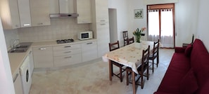A kitchen with a dining area, a red sofa, and a window with curtains. - Experience Comfort by the Coast-beahost Rentals (Rosolina)