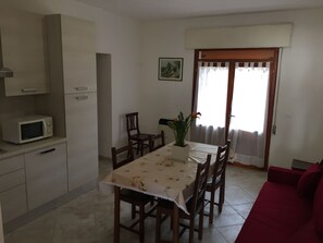 A dining area with a table, chairs, a microwave, and a red sofa. - Experience Comfort by the Coast-beahost Rentals (Rosolina)
