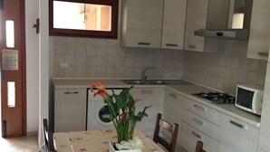 Ett kök med vita skåp, en mikrovågsugn och en spis. Där finns ett matbord med stolar och en vas med blommor.