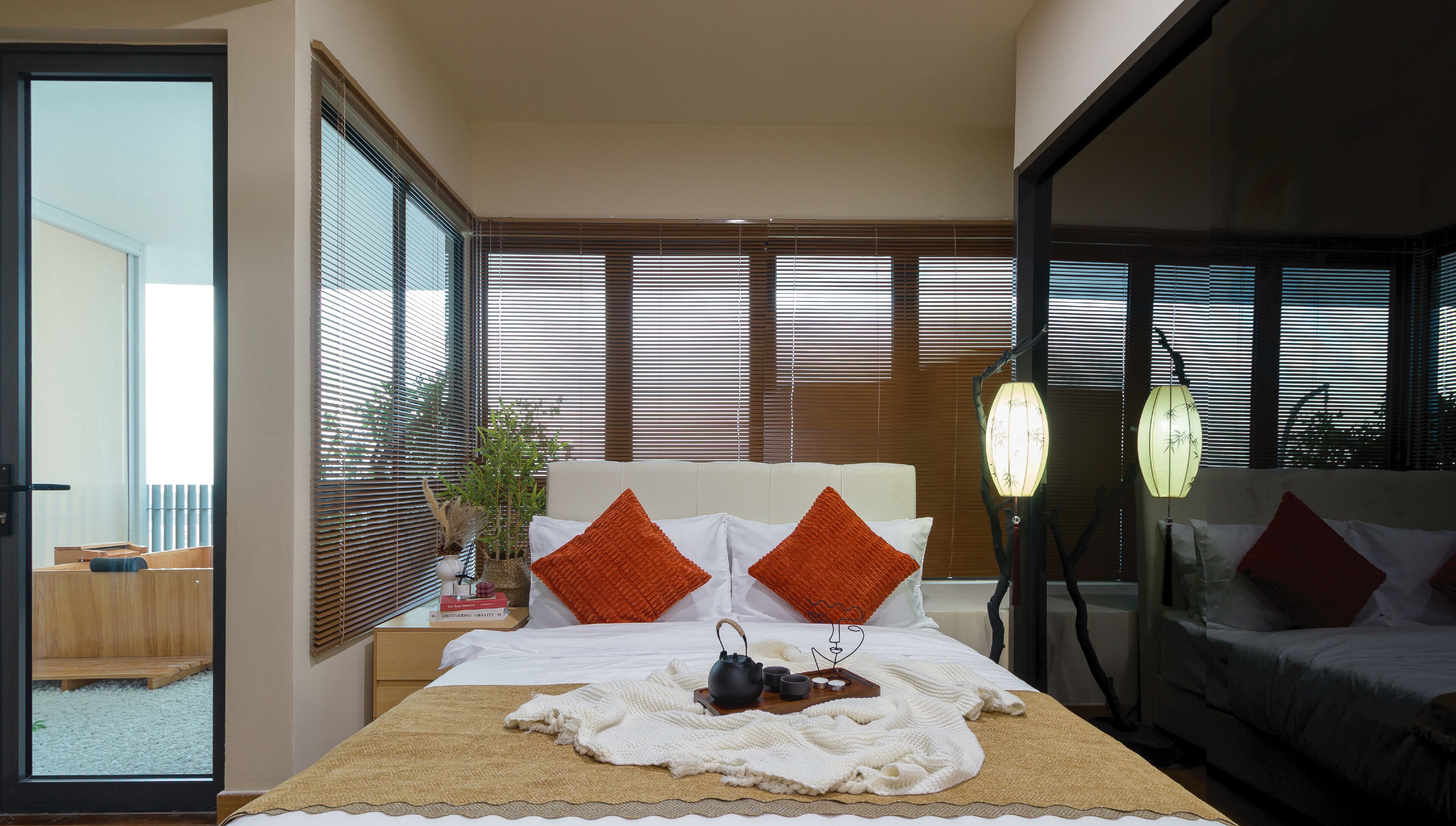 A modern hotel room with a large bed, a bedside table with a lamp, and a view of the outside balcony.