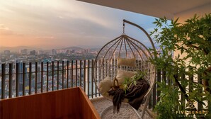 Quarto com cadeira suspensa, vista para a cidade e uma planta.