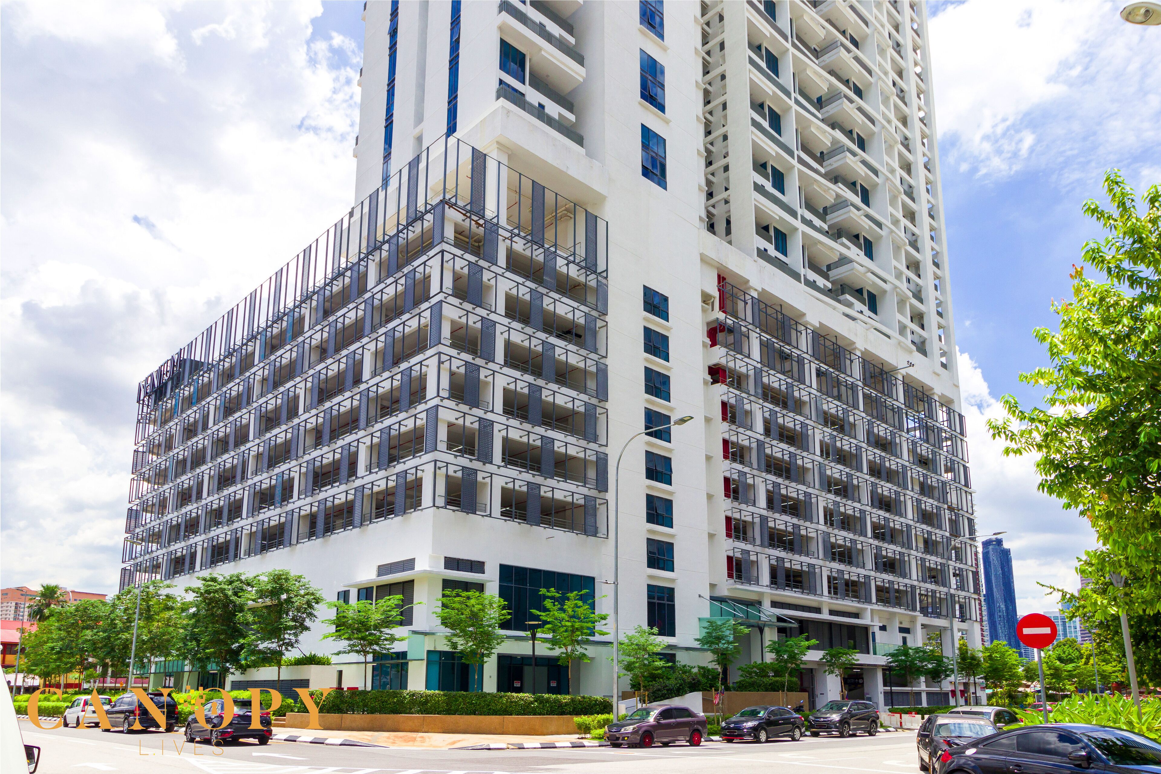 A multi-story building with balconies, a street in front, and a clear sky.