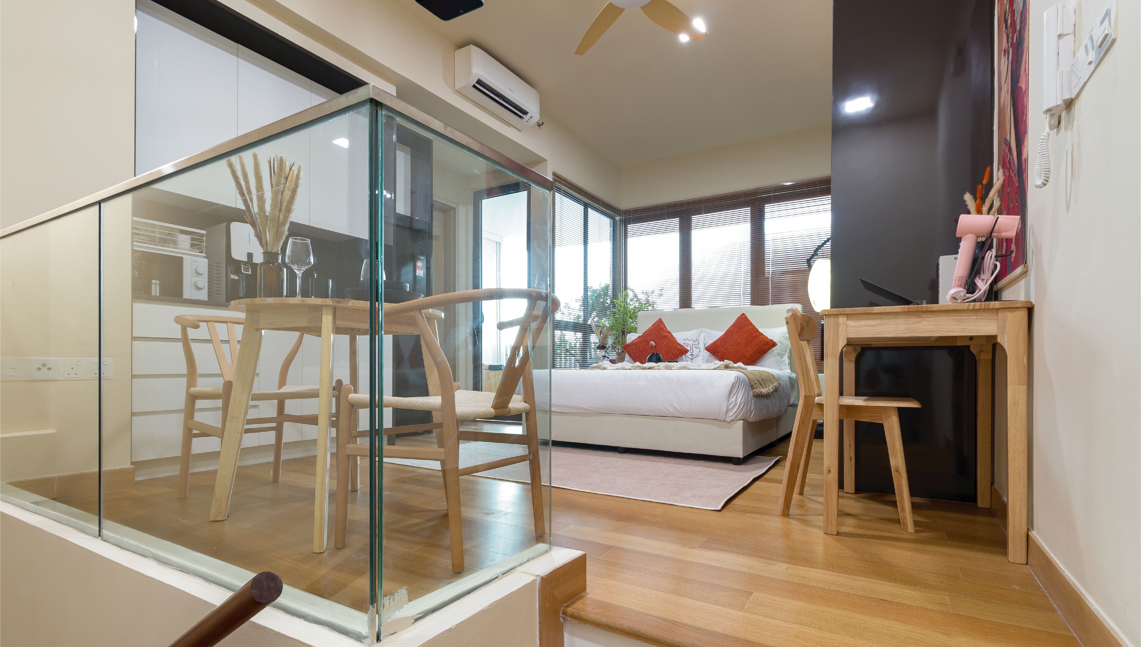 A modern living room with a glass partition, wooden furniture, and a bed with red pillows.