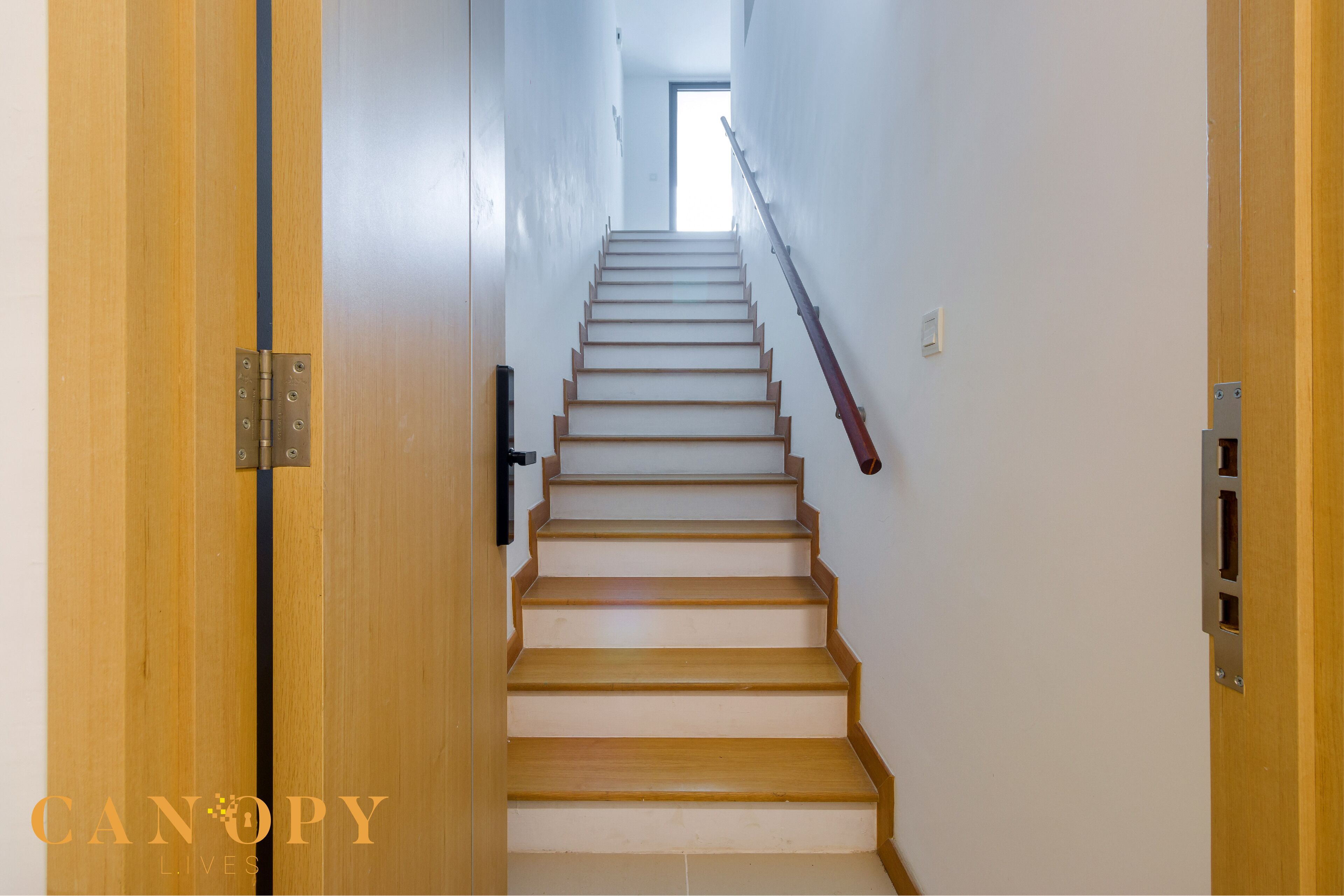 Una escalera de madera que lleva a un rellano con una puerta a la izquierda.