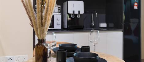 A modern kitchen with a round wooden table set for dining, featuring black bowls and glasses, and a vase with dried plants.