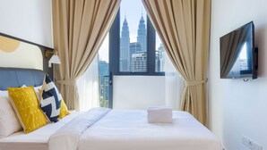 Quarto de hotel com uma cama, cortinas, televisão e vista para a paisagem urbana.