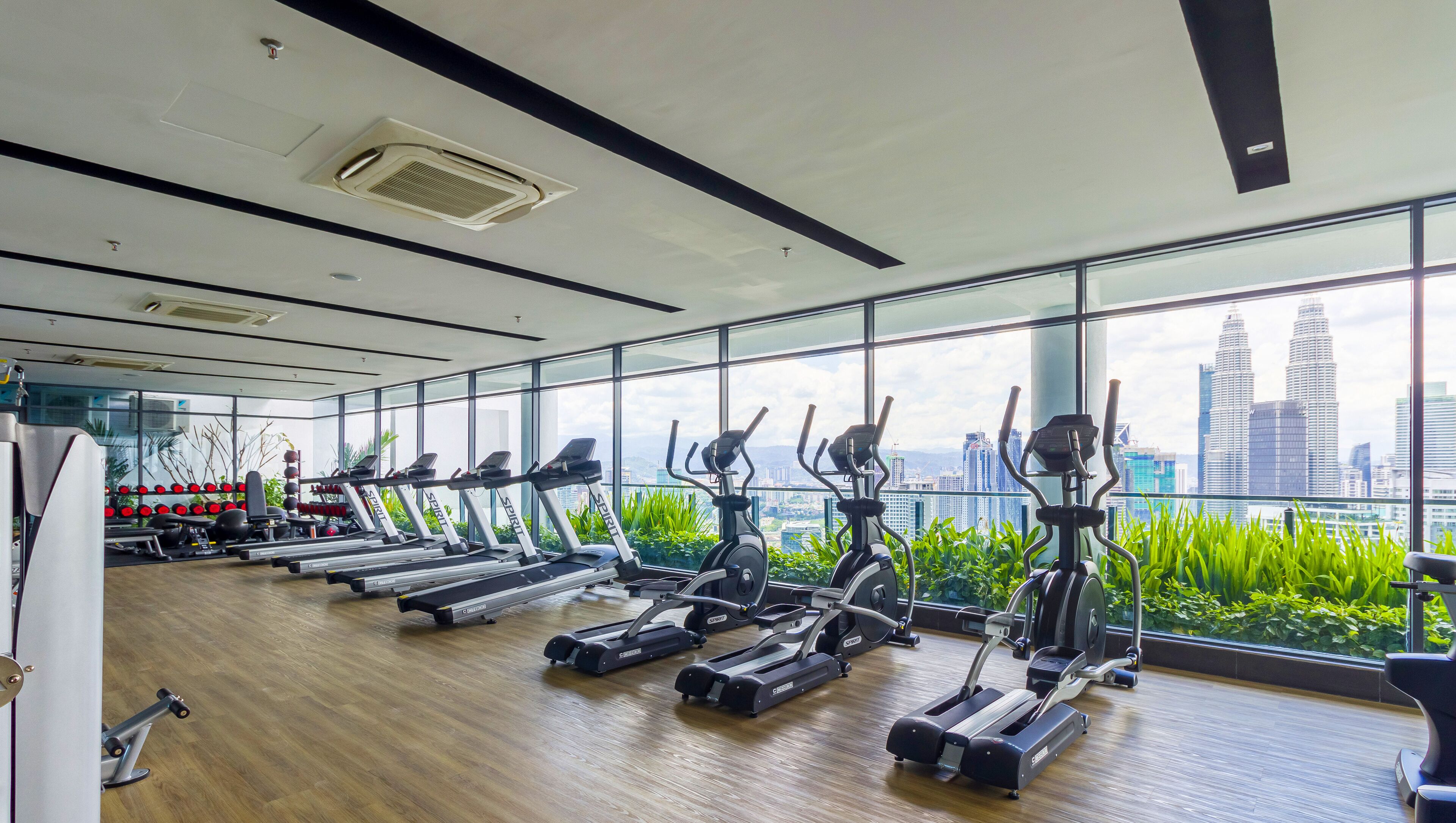 Ein modernes Fitnessstudio mit mehreren Cardiogeräten, großen Fenstern und Blick auf die Stadt sowie einem sauberen Holzboden.
