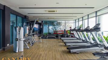 Un gimnasio moderno con diversos equipos de ejercicio, incluyendo cintas de correr y máquinas de pesas, con ventanas amplias y suelo de madera.