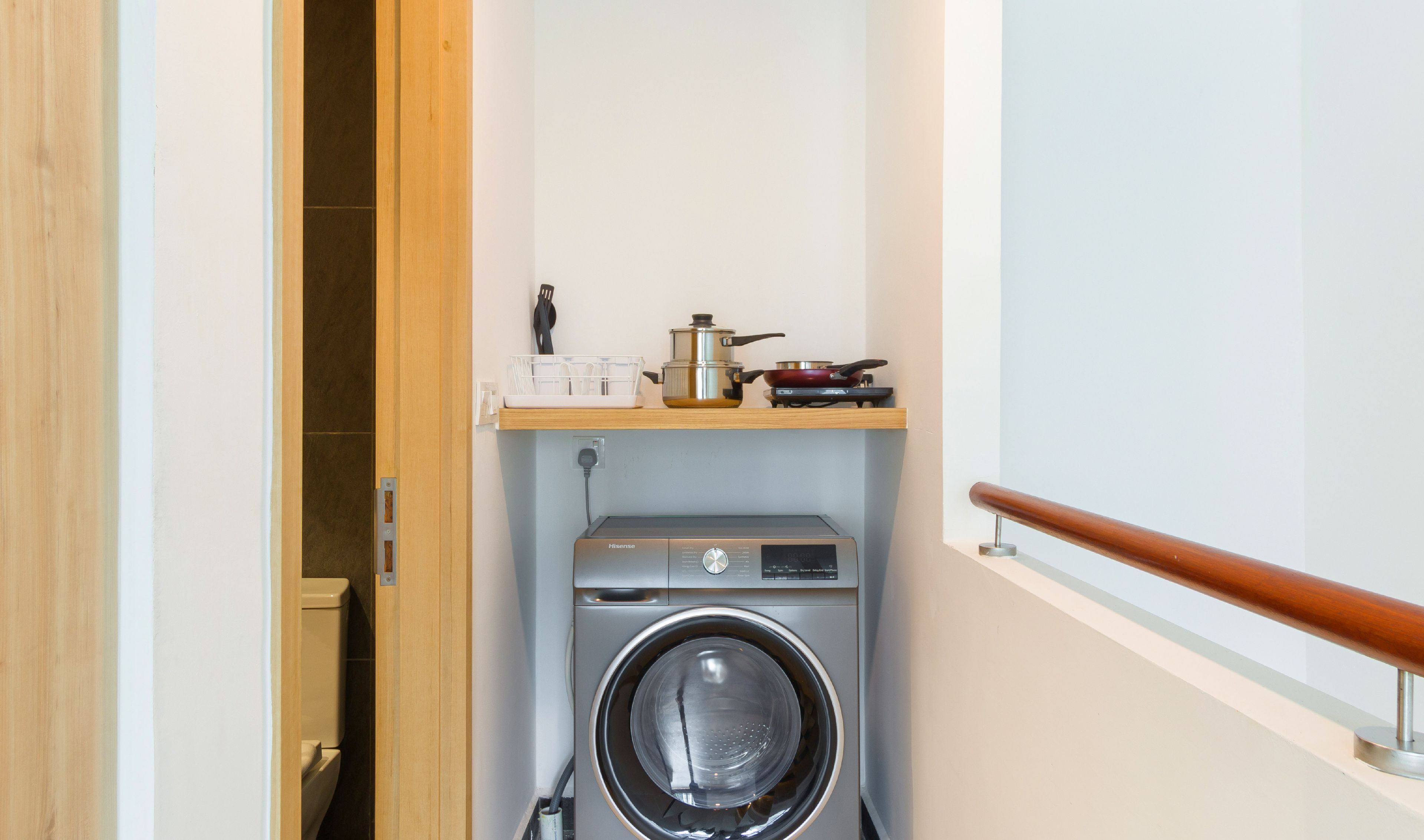 Un espace buanderie compact comprenant un lave-linge, une étagère avec des ustensiles de cuisine et une porte en bois.