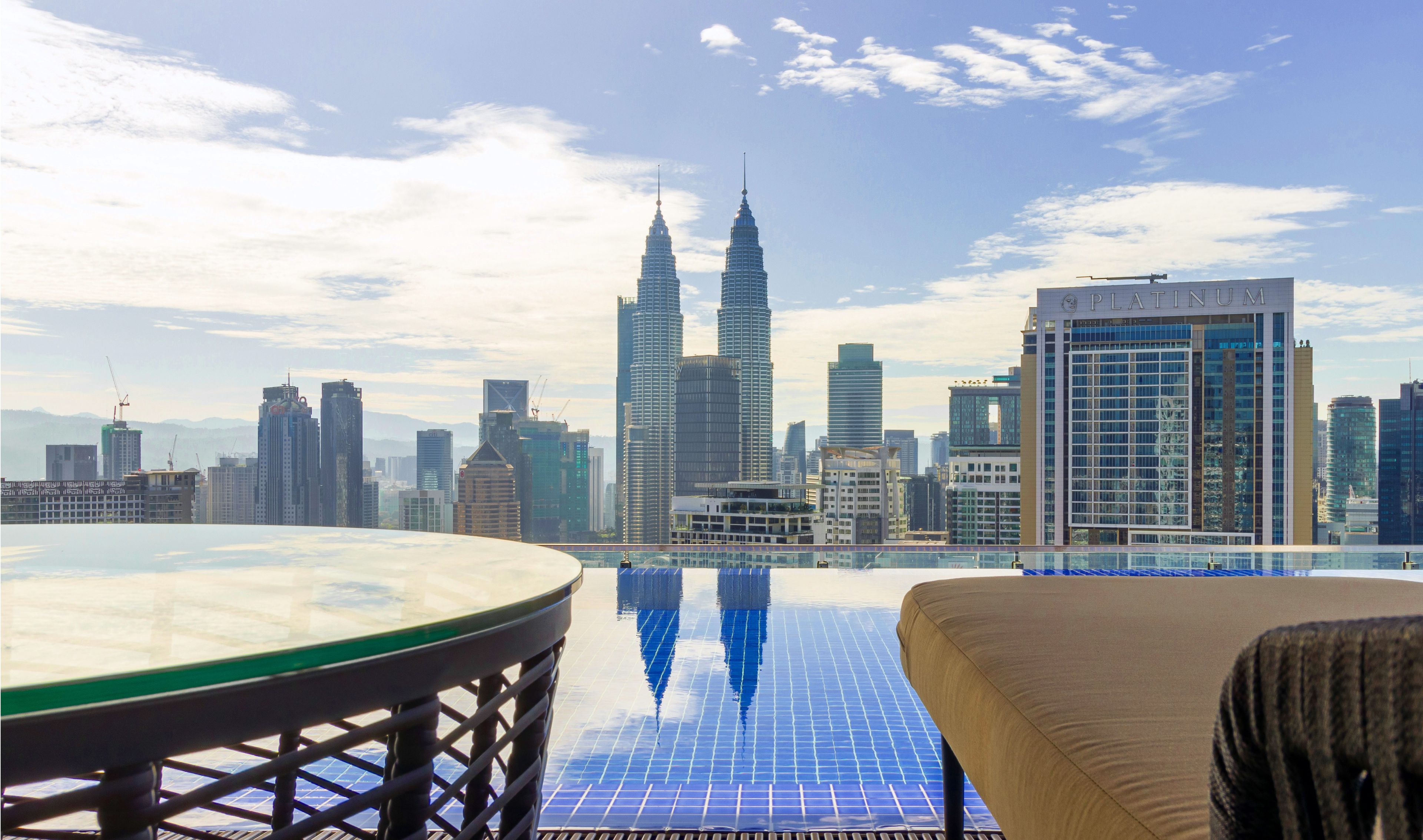 A rooftop terrace with a glass table and a view of the city skyline, including the Petronas Twin Towers and the Platinum building.