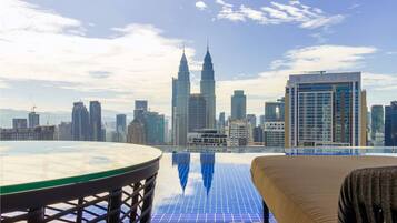 A rooftop terrace with a glass table and a view of the city skyline, including the Petronas Twin Towers and the Platinum building.