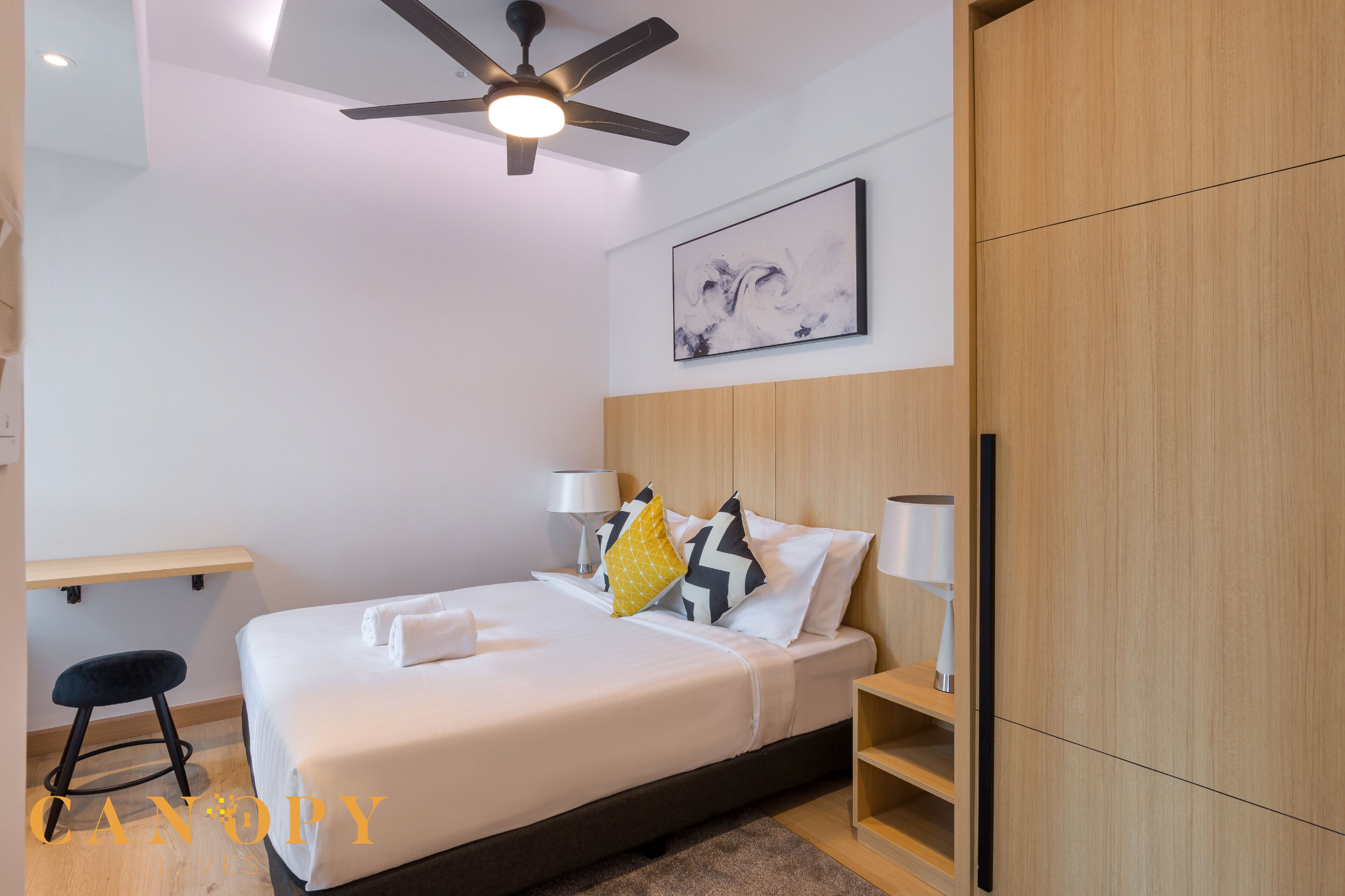Habitación de hotel moderna con cama, ventilador de techo, mesita de noche, lámpara, silla y armario.