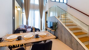 Uma sala de jantar moderna com uma mesa de madeira posta para quatro pessoas, um sofá e uma escada com grades de vidro.