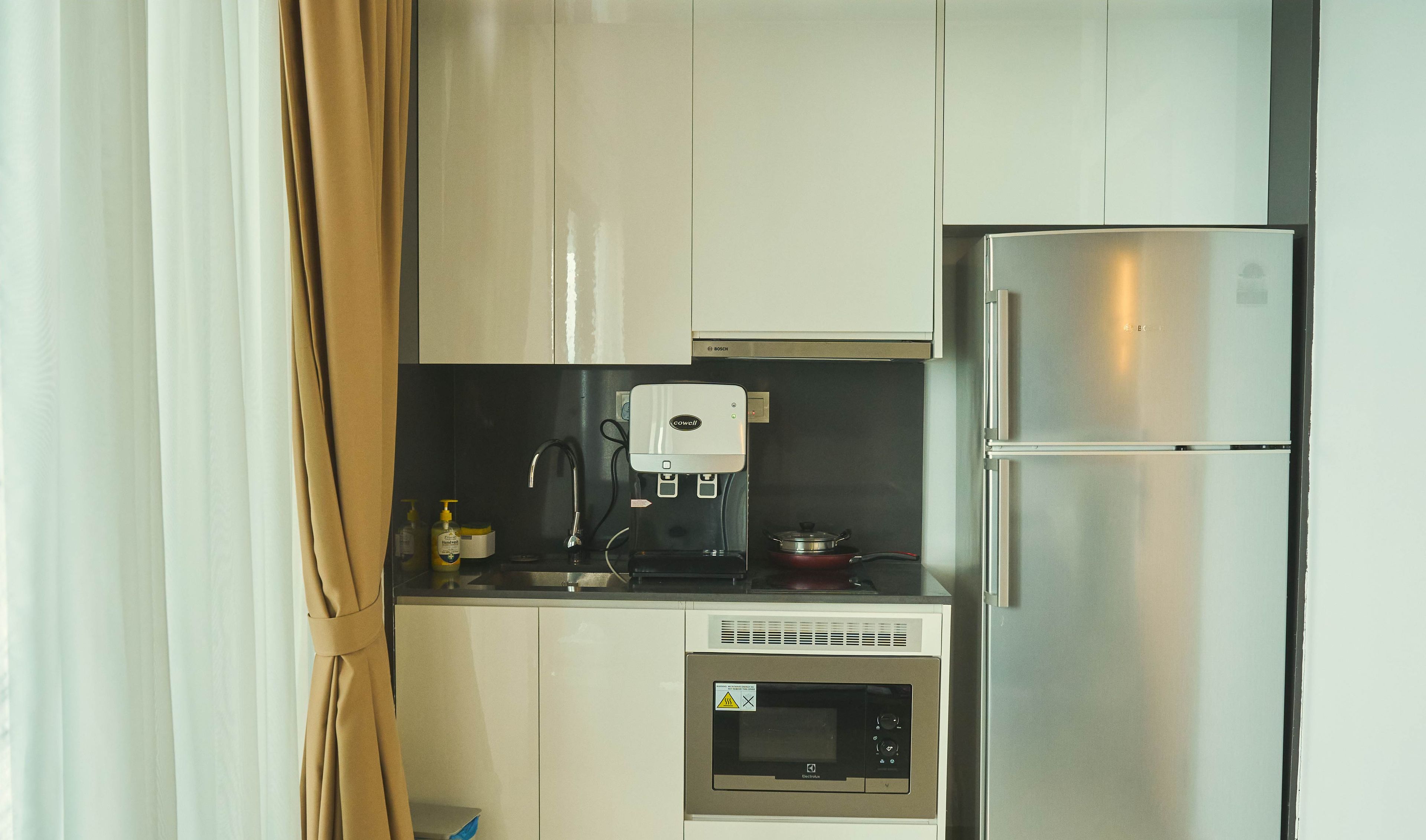 A compact kitchen with white cabinets, a stainless steel refrigerator, a microwave, and a coffee maker.