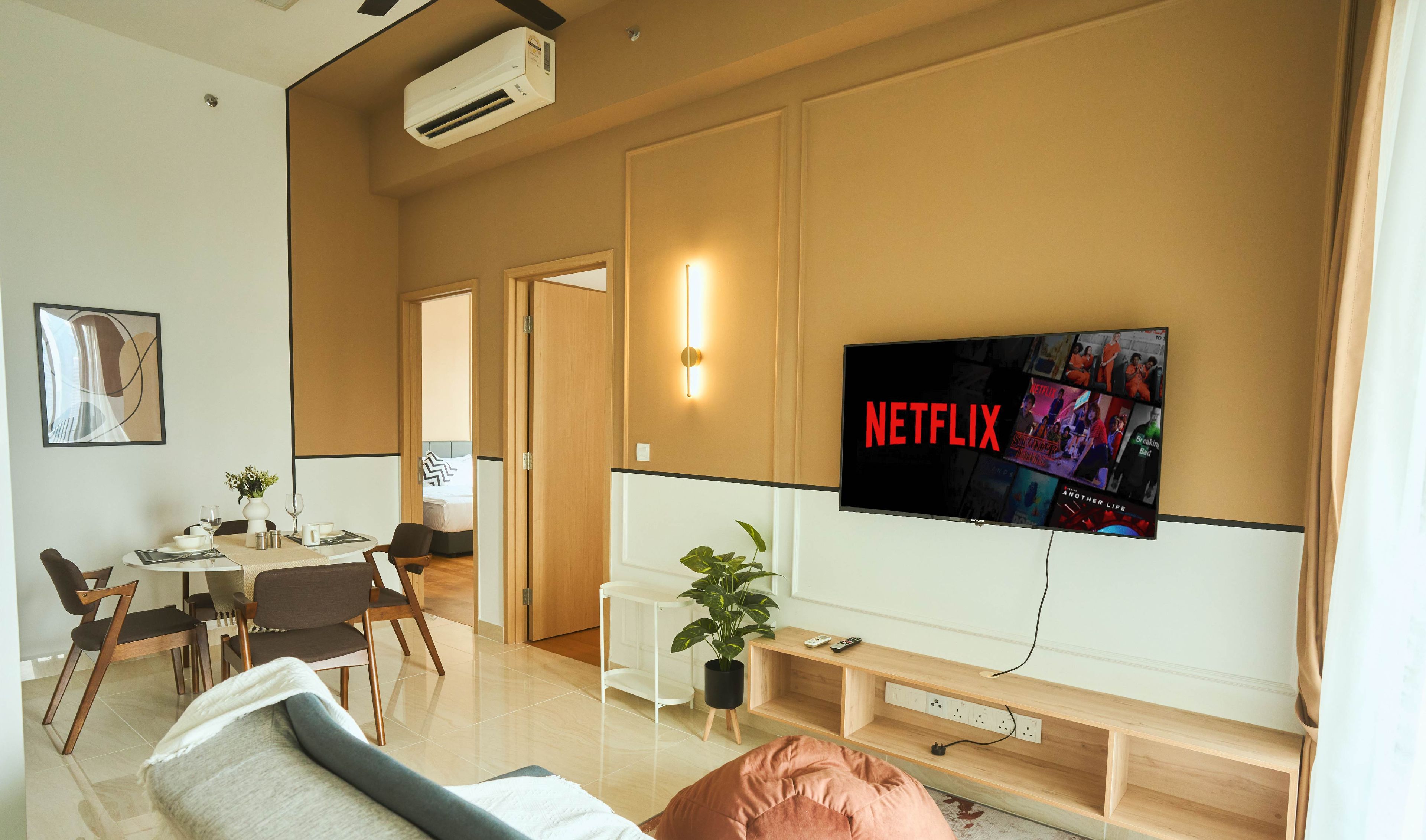 Een moderne woonkamer met een flatscreen televisie aan de wand, een bank, een eethoek met een tafel en stoelen, en een kamerplant.