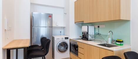 A compact kitchen with a washing machine, a refrigerator, a coffee maker, and a sink.