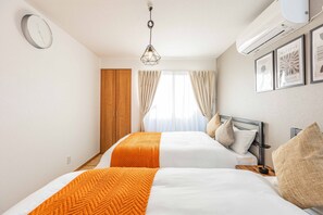 A hotel room with two beds, a wooden wardrobe, a window with curtains, a wall-mounted clock, and framed artwork. - Fleur Sanno (Osaka)