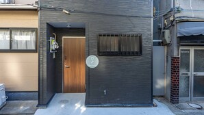 A modern building with a dark facade, a wooden door, and a small window with bars. - Fleur Sanno (Osaka)