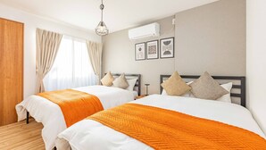A hotel room with two beds, beige curtains, a hanging light fixture, and an air conditioning unit on the wall. - Fleur Sanno (Osaka)