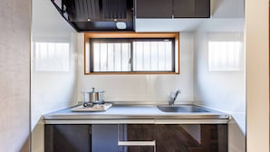 A compact kitchen with a window above the sink, a stove, and a cabinet below. - Fleur Sanno (Osaka)