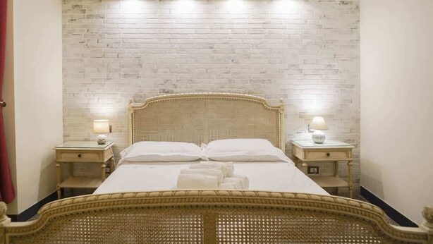 Una cama bien hecha con un cabecero tejido, dos mesitas de noche con lámparas y una pared de ladrillo blanco con diseño.