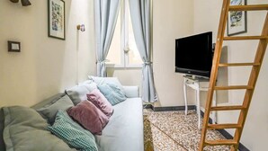 Una habitación con sofá, televisor, escalera y ventana con cortinas.