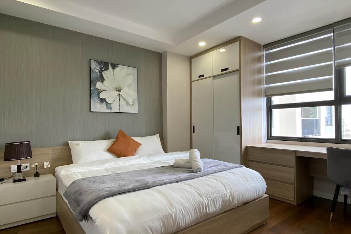 A modern bedroom with a large bed, a desk, and a wardrobe.