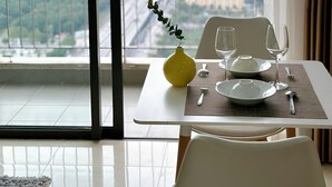A dining area with a table set for two, a yellow vase, and a city view through large windows. - Vinhomes D'Capitale Ha Noi-Gem Apartment (Hanoi)