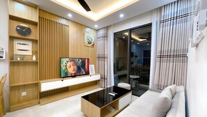 A modern living room with a flat-screen TV, wooden shelving, a sofa, and a ceiling fan. - Vinhomes D'Capitale Ha Noi-Gem Apartment (Hanoi)
