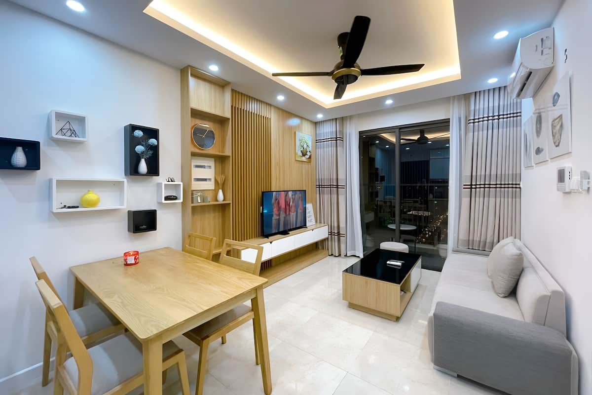 A modern living room with a wooden dining table, a sofa, a TV, and a ceiling fan.