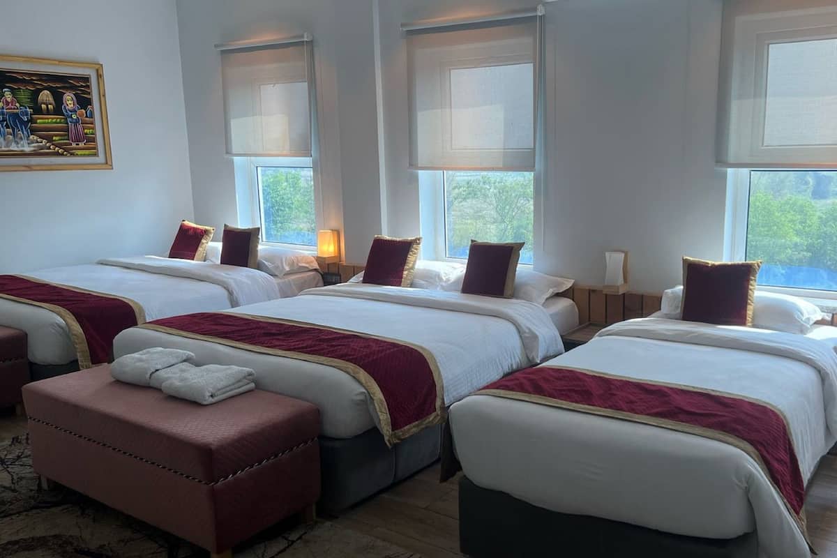 Une chambre d’hôtel avec trois lits, un coin salon et de grandes fenêtres donnant sur un paysage verdoyant.