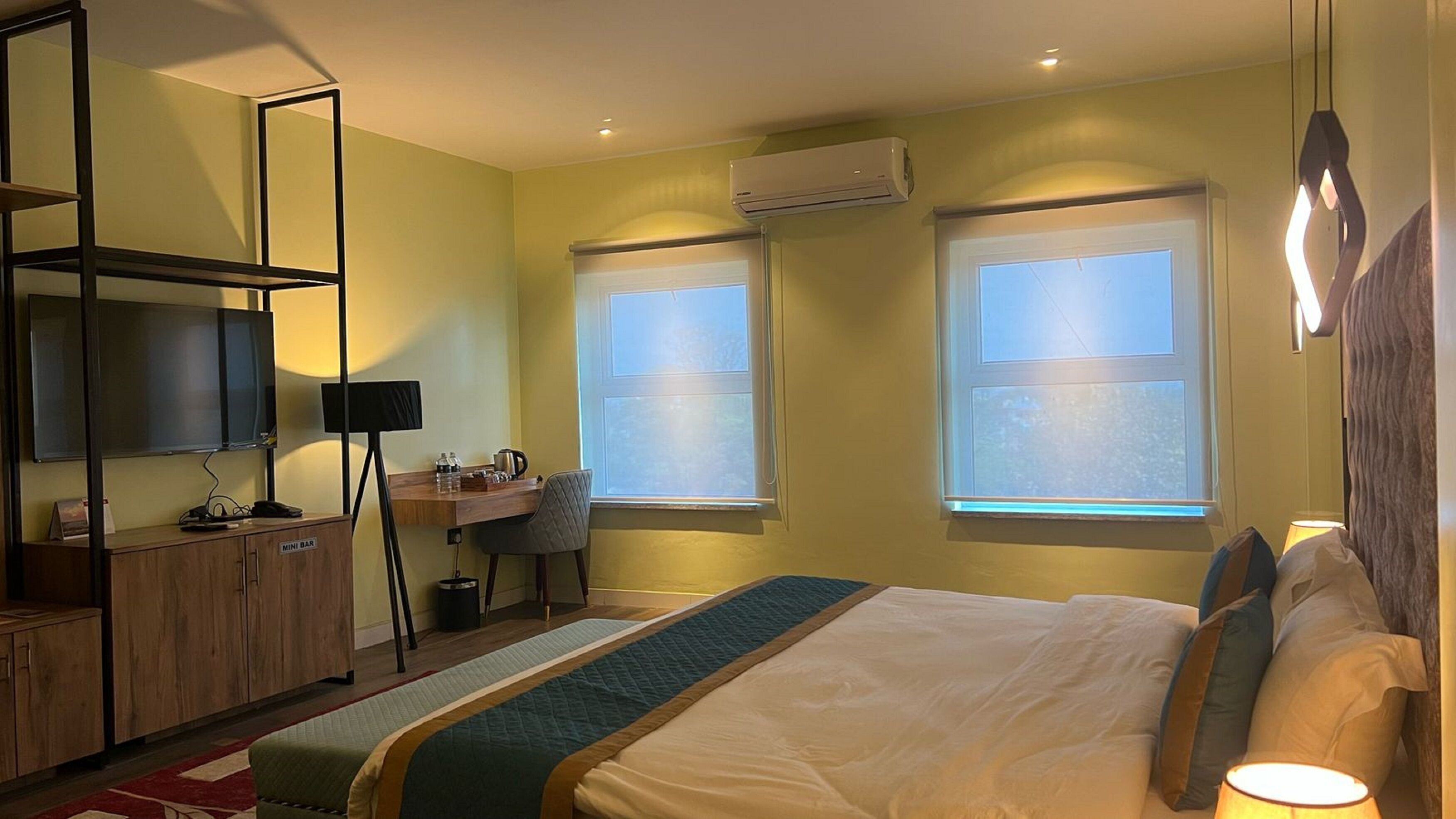 A hotel room with a bed, a desk, a TV, and a minibar.