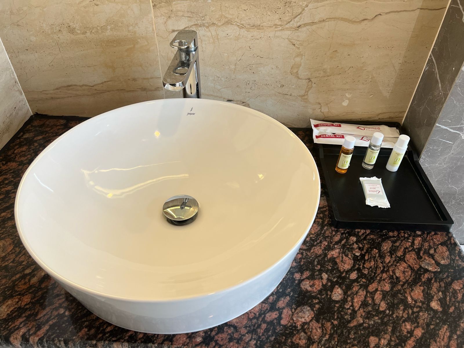A white vessel sink with a single faucet, a black tray with dental care products, and a marble wall.