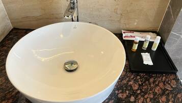 A white vessel sink with a single faucet, a black tray with dental care products, and a marble wall.
