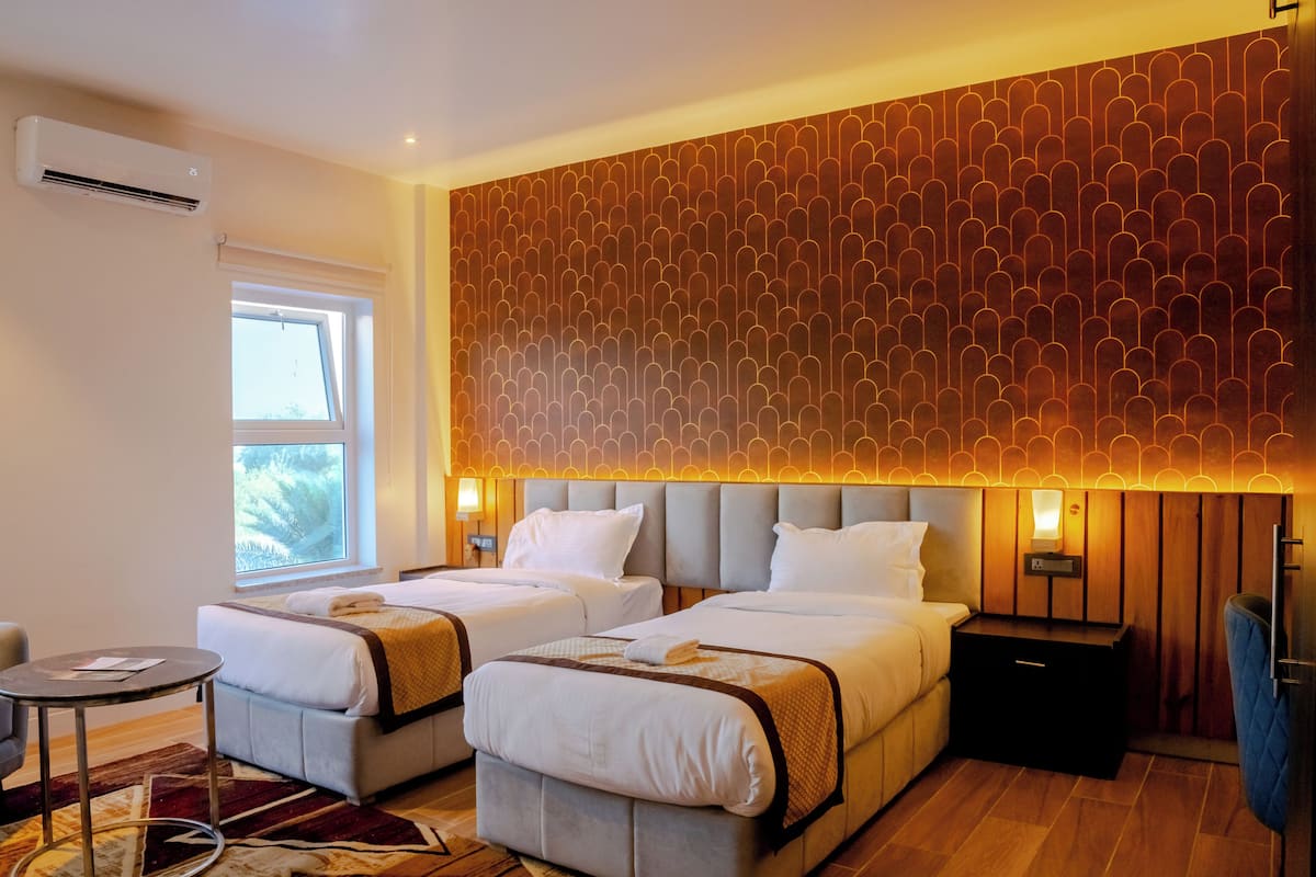 Une chambre d’hôtel avec deux lits, une petite table, une chaise, une table de chevet et une fenêtre donnant sur un paysage agréable.