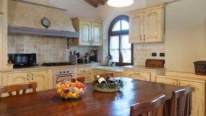 A kitchen with wooden cabinets, a stove, a microwave, and a dining table with chairs. - Rustikale Villa mit Privat Pool in Buti, Toscana. Haustierfreundlich (Buti)