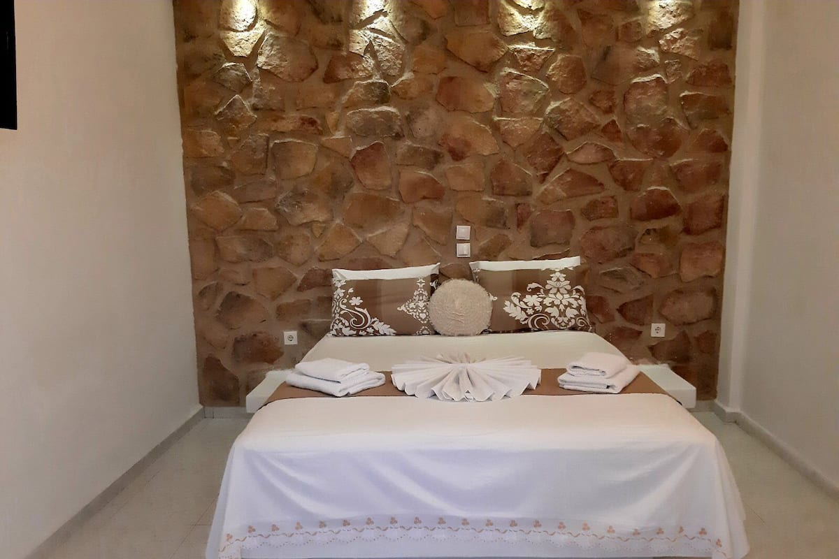 A neatly made bed with a white bedspread and decorative pillows, set against a stone wall.