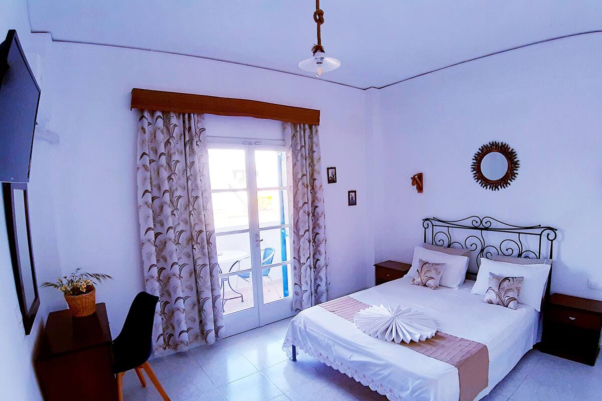 A bedroom with a bed, a desk, a chair, a TV, and a window with curtains.