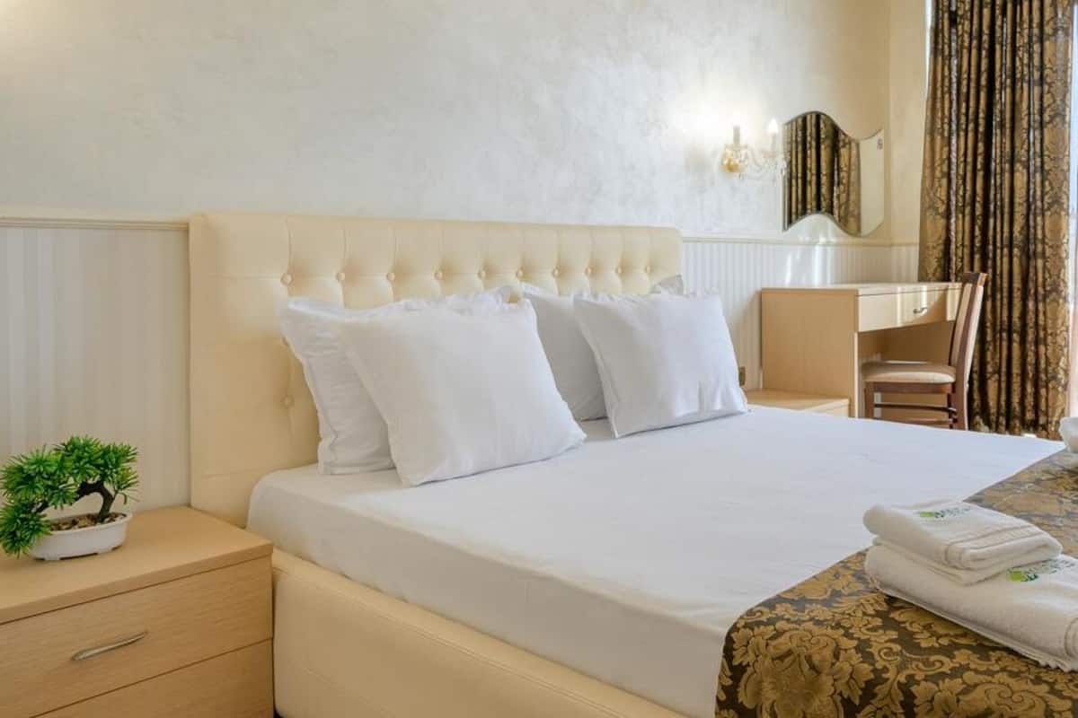 A hotel room with a large bed, a desk, a chair, a small plant, and a window with curtains.