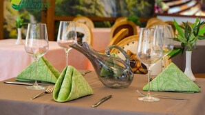 A table set with green napkins, clear wine glasses, and a clear pitcher, with a painting and wooden clocks in the background. - Allegra Balneo & SPA (Golden Sands)