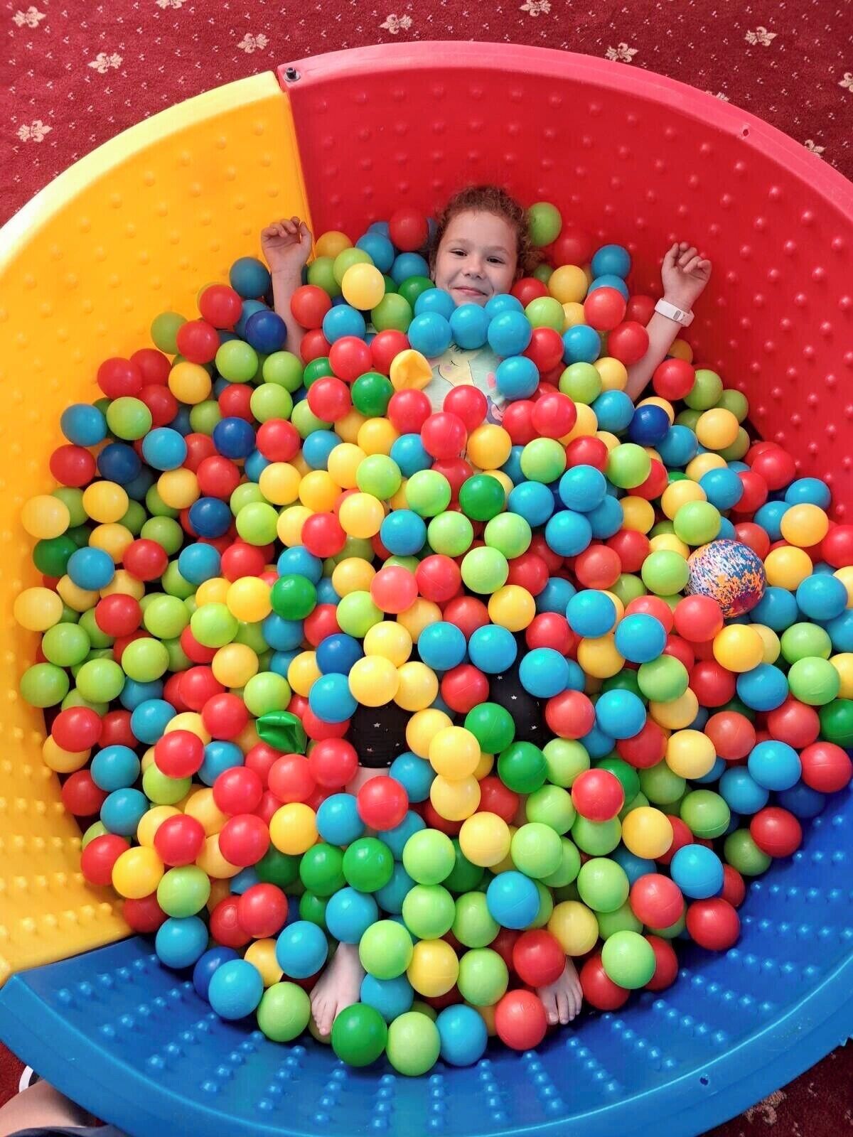 A child surrounded by colorful plastic balls in a play area.