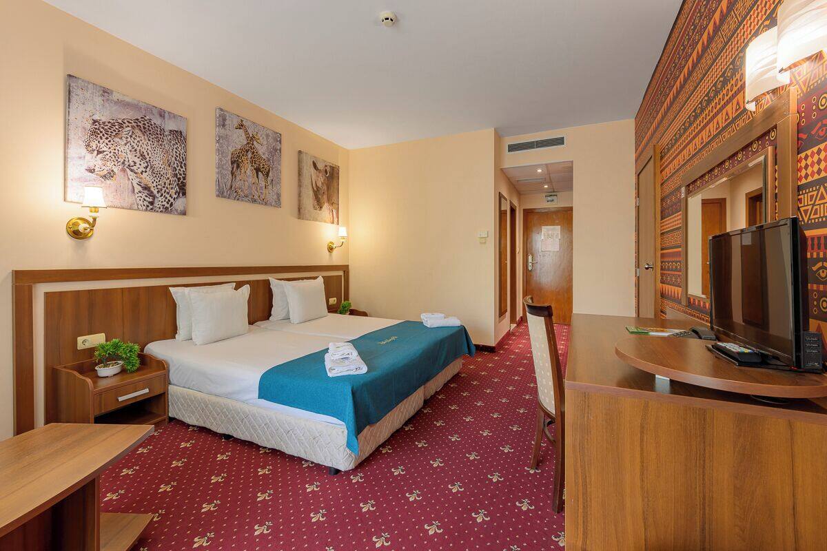 A hotel room with a large bed, a desk with a television, and artwork on the walls.