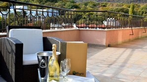 A balcony with wicker furniture, a bottle of wine, and glasses on a table, overlooking a scenic landscape. - Allegra Balneo & SPA (Golden Sands)