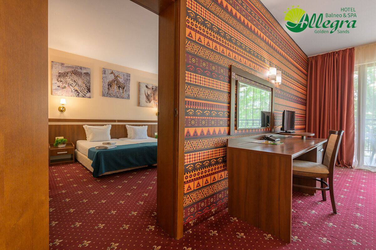 A hotel room with a bed, desk, and a patterned wall.