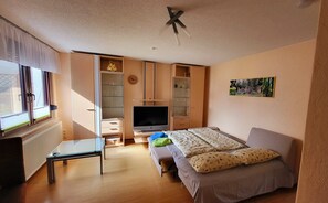 Ein Schlafzimmer mit Bett, Fernseher, Schreibtisch und Kleiderschrank.