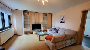 Ein Wohnzimmer mit einer Couch, einem Fernseher und offenen Regalen.